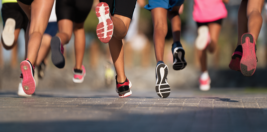 sept personnes sont en train de courir sur du bitume, cinq d'elles ont des baskets de running roses, deux ont des baskets rouges, une personne a des baskets de running noire et une blanche