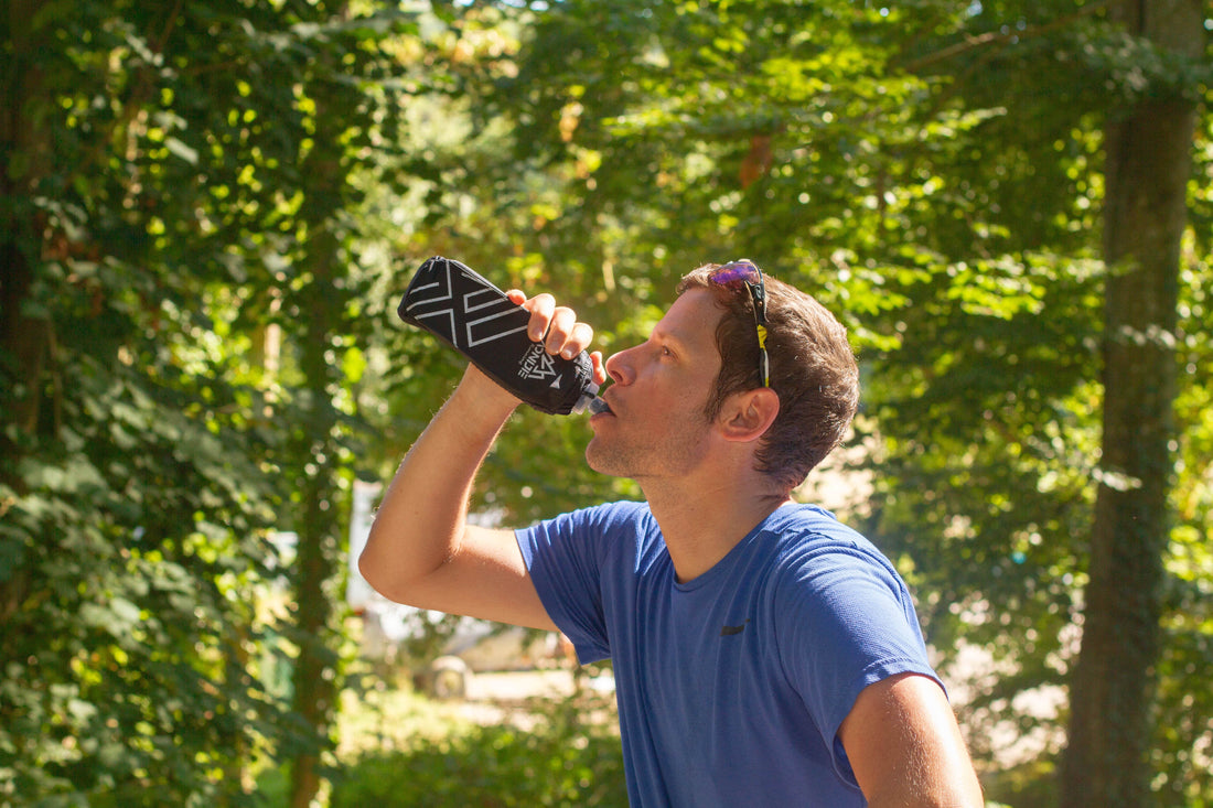 Un homme avec un t-shirt bleu boit dans sa gourde running au milieu d'une forêt