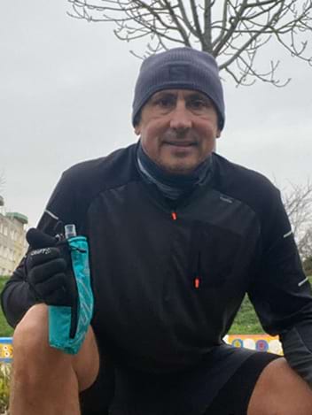 Un homme en tenue de sport chaude est accroupi durant une journée grise et tiens une gourde running bleue dans sa main droite