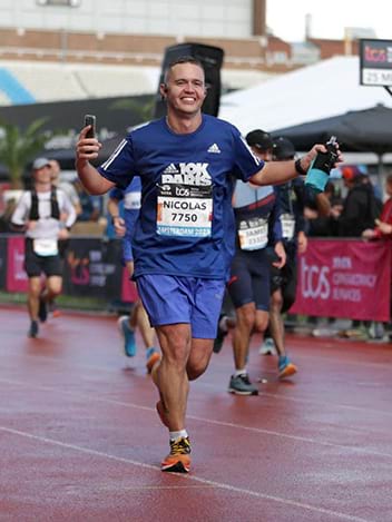 Un homme en tenue de sport entièrement bleue est en train de courir lors d'un marathon sur une piste de course à pied, il tiens une gourde running bleue dans sa main gauche