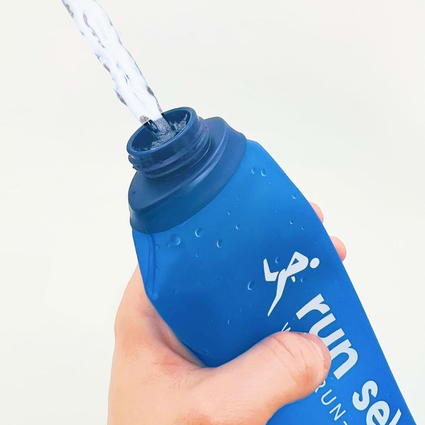 Une flasque bleue run select est pressée par une main pour faire jaillir de l'eau vers le haut